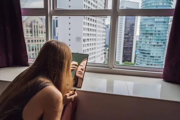 Jeune femme se maquille assis près de la fenêtre avec une vue panoramique sur les gratte-ciel et la grande ville — Photo