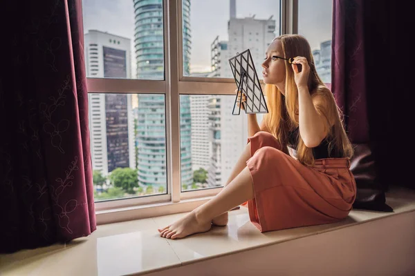 Jeune femme se maquille assis près de la fenêtre avec une vue panoramique sur les gratte-ciel et la grande ville — Photo