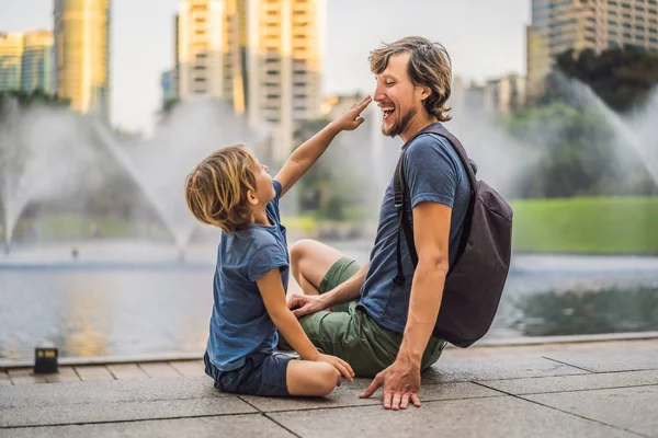 Táta a syn turistů na pozadí fontány na jezeře v noci, v blízkosti Twin Towers s městem v pozadí. Kuala Lumpur, Malajsie — Stock fotografie