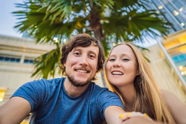 Viajes, vacaciones y concepto de vacaciones - Pareja feliz divirtiéndose tomando selfie sobre el parque con fondo de palmeras y rascacielos — Foto de Stock