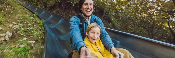 Dad and son have fun on alpine roller coaster BANNER, LONG FORMAT