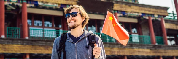 Enjoying vacation in China. Young man with national chinese flag on the background of the old Chinese street. Travel to China concept. Visa free transit 72 hours, 144 hours in China. BANNER, LONG