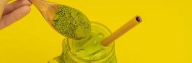 Mason kavanoza ve saman ve tozu matcha sarı zemin üzerine kaşıkla buzlu yeşil çay latte. Ev yapımı buzlu Matcha Latte sütlü çay sıfır atık afiş, uzun biçimde