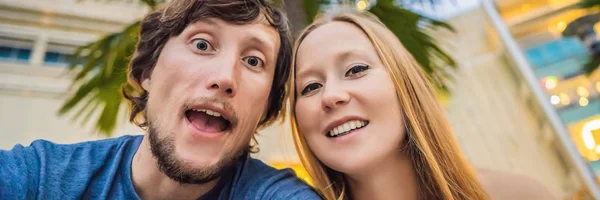 Viajes, vacaciones y concepto de vacaciones - Pareja feliz divirtiéndose tomando selfie sobre el parque con palmeras fondo y rascacielos BANNER, FORMATO LARGO — Foto de Stock