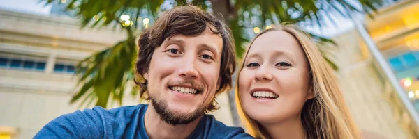 Viajes, vacaciones y concepto de vacaciones - Pareja feliz divirtiéndose tomando selfie sobre el parque con palmeras fondo y rascacielos BANNER, FORMATO LARGO — Foto de Stock