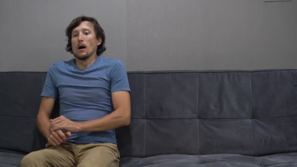 Un jeune homme s'assoit sur un canapé et se sent déprimé et effrayé. Copier l'espace sur le côté droit — Video