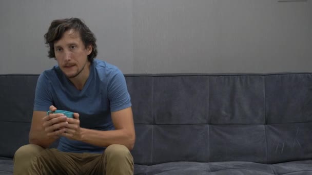 A young man sits on a couch and feels frustrated, depressed and fear. He tries to drink some water or tea to calm down. Copy space on the right side — Stock Video