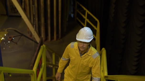 Молода людина в жовтій робочій формі, окулярах і шоломі в промисловому середовищі, нафтовій платформі або на зрідженому газовому заводі. Постріл уповільнення — стокове відео