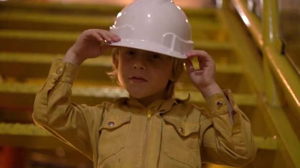 一个穿着黄色工作服、头盔的小男孩在工业环境中的慢镜头, 石油平台或液化气厂坐在楼梯上。慢镜头 — 图库视频影像