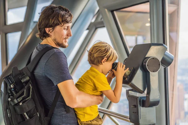 Dad and son are looking at Kuala lumpur cityscape. Use binoculars. Panoramic view of Kuala Lumpur city skyline evening at sunset skyscrapers building in Malaysia. Traveling with kids concept — Stock Photo, Image