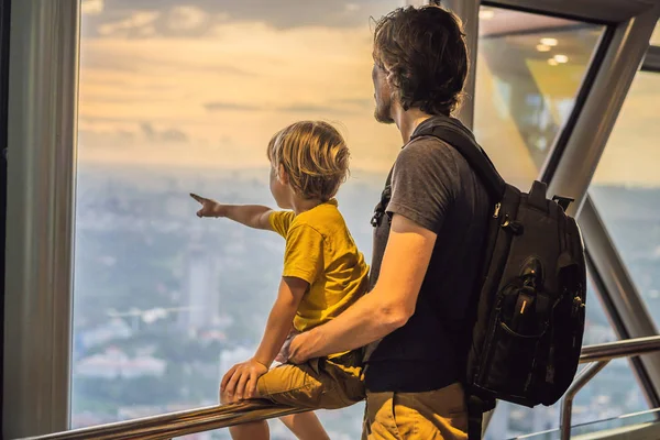 Vader en zoon kijken Kuala lumpur stadsgezicht. Panoramisch zicht van Kuala Lumpur stad skyline avond bij zonsondergang wolkenkrabbers bouwen in Maleisië. Reizen met kids concept — Stockfoto