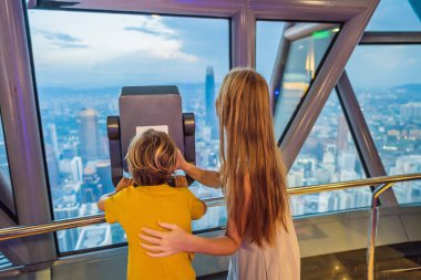Anne ve oğlu Kuala lumpur cityscape arıyoruz. Dürbün kullanın. Gün batımı gökdelenler içinde Malaysia bina panoramik manzaraya Kuala Lumpur şehir manzarası akşam. Çocuklar kavramı ile seyahat