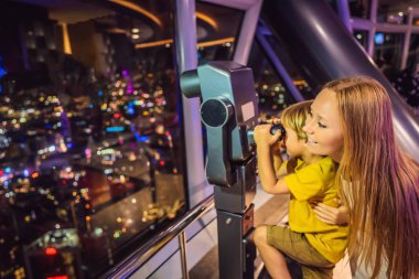 Anne ve oğlu Kuala lumpur cityscape arıyoruz. Dürbün kullanın. Gün batımı gökdelenler içinde Malaysia bina panoramik manzaraya Kuala Lumpur şehir manzarası akşam. Çocuklar kavramı ile seyahat