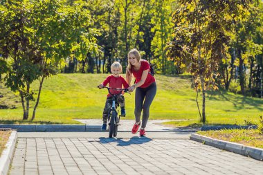 Genç Anne oğlunu parkta Bisiklete binmek kullanmayı öğretmek