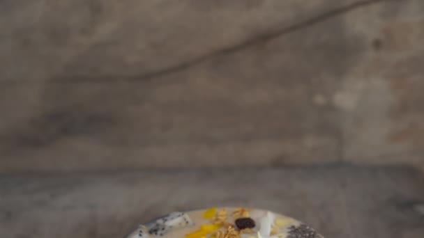 드래곤 과일, 망고, 그 라 놀라, 건포도, 아몬드 슬라이스, 그리고 나무 배경에 chia 씨앗 바나나 스무디 그릇 — 비디오
