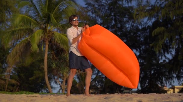 Βολή slowmotion Α νέος άνθρωπος φουσκώνει ένα φουσκωτό καναπέ σε μια όμορφη παραλία — Αρχείο Βίντεο