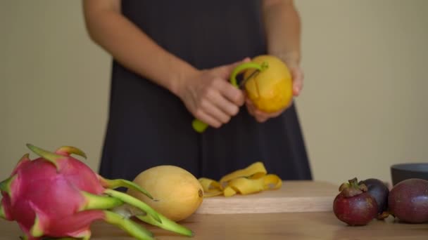 4x vezes Slowmotion tiro de uma jovem mulher descascando a manga e muitas frutas tropicais estavam em uma mesa — Vídeo de Stock