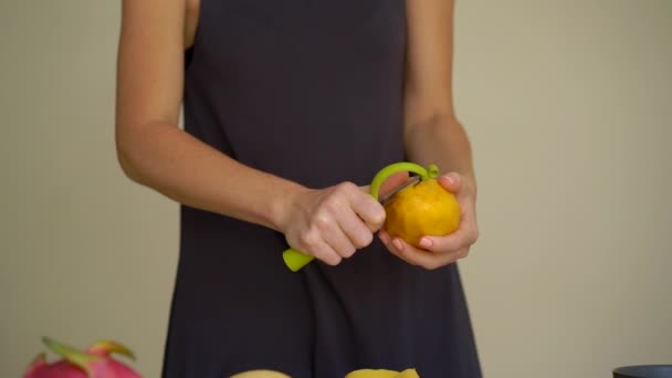 В 4 раза медленный снимок молодой женщины, очищающей манго и много тропических фруктов лежал на столе — стоковое видео