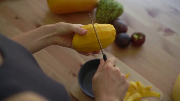 4x veces Lento disparo de una mujer joven cortando el mango en cubos y un montón de frutas tropicales yacen en una mesa — Vídeo de stock