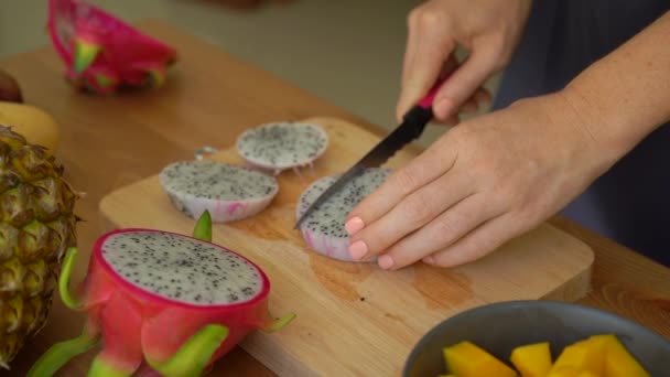 2x times Slowmotion shot of a young woman cutting the dragon fruit into cubes and lots of tropical fruits lay on a table — Stock Video