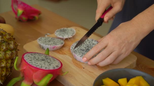 4x vezes Slowmotion tiro de uma jovem mulher cortando a fruta do dragão em cubos e muitas frutas tropicais estavam em uma mesa — Vídeo de Stock