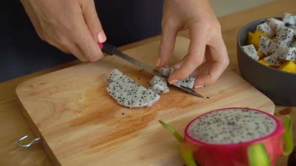 2x vezes Slowmotion tiro de uma jovem mulher colocando os cubos de frutas do dragão em uma tigela de cerâmica cinza e muitas frutas tropicais estavam em uma mesa — Vídeo de Stock