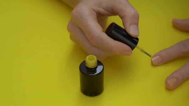 Närbild bild av en flicka som målar sina naglar i gult på en gul bakgrund. Gula koncept. — Stockvideo