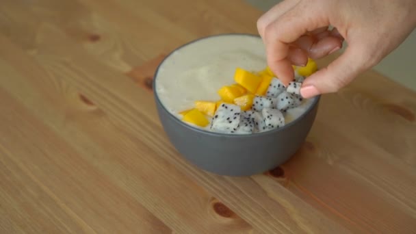 Slowmotion skott av en ung kvinna matlagning banana smoothie bowl med dragon frukt, mango, granola, russin, mandel skivor och chiafrön — Stockvideo