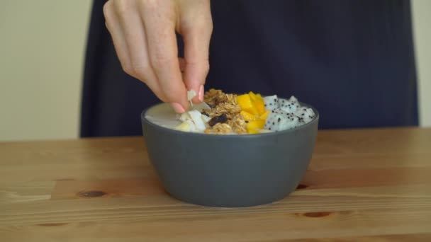 Slowmotion shot of a young woman cooking banana smoothie bowl with dragon fruit, mango, granola, raisin, almond slices, and chia seeds — Stock Video