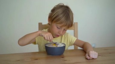 Superslowmotion shot dragon meyve, mango, granola, Kuru üzüm, badem dilimleri ve chia tohum ile bir muz smoothie kase yemek küçük bir çocuk