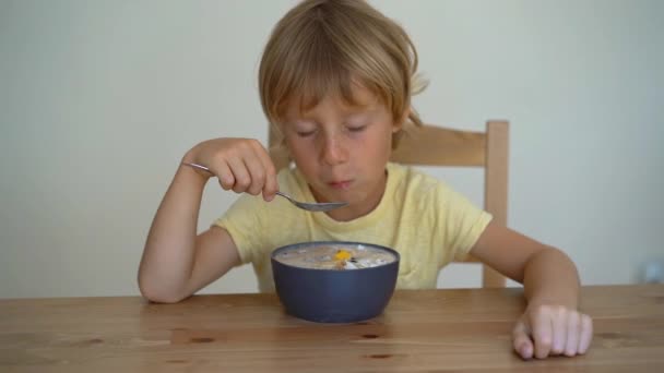 Superslowmotion στιγμιότυπο από ένα μικρό αγόρι τρώει μια μπανάνα μπολ smoothie με φρούτα δράκος, μάνγκο, granola, σταφίδα, αμύγδαλο φέτες και τους σπόρους chia — Αρχείο Βίντεο