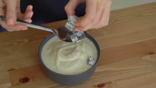 En ung kvinna som matlagning banana smoothie bowl med dragon frukt, mango, granola, russin, mandel skivor och chiafrön — Stockvideo