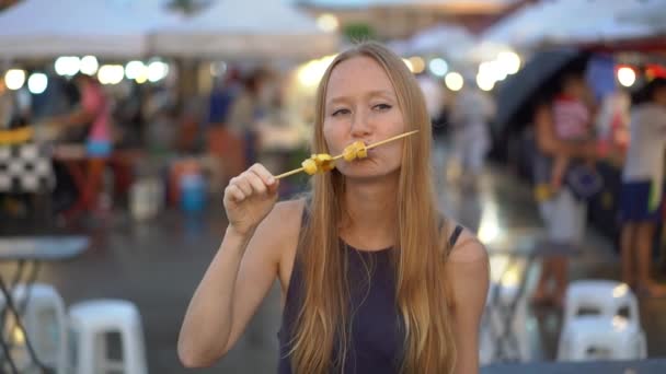 Zeitlupenaufnahme einer jungen Frau, die Streetfood auf einem asiatischen Wochenmarkt isst — Stockvideo