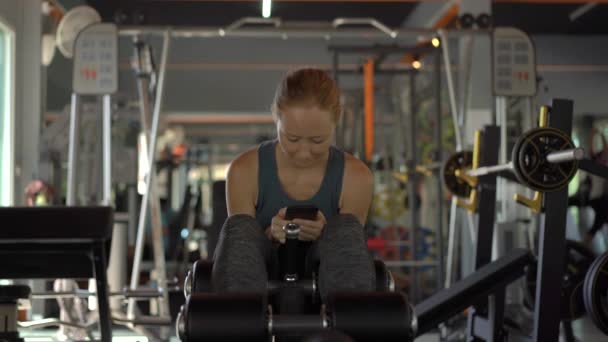 Slowmotion skott av en ung kvinna på gymmet skakar pressen håller telefonen framför hennes ögon i hennes händer. All uppmärksamhet är i telefonen. Begreppet beroende på sociala nätverk — Stockvideo