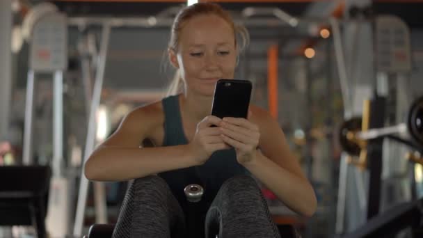 Slowmotion skott av en ung kvinna på gymmet skakar pressen håller telefonen framför hennes ögon i hennes händer. All uppmärksamhet är i telefonen. Begreppet beroende på sociala nätverk — Stockvideo