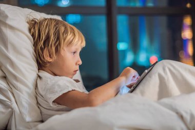 Çocuk tablet yatağında gitmeden önce bir gece şehir bir arka plan üzerinde uyku için kullanır. Çocuk ve teknoloji kavramları