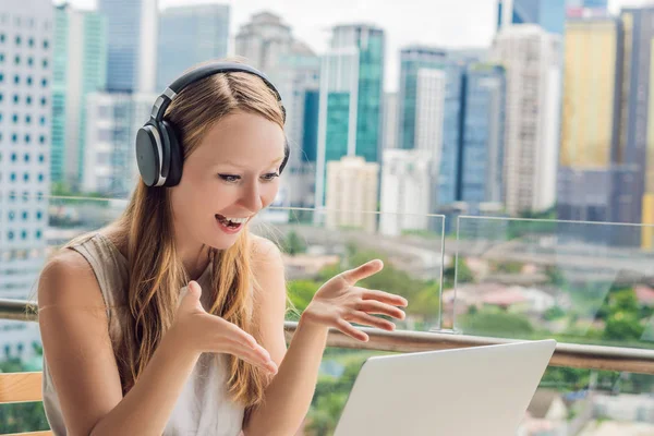 Young woman teaches a foreign language or learns a foreign language on the Internet on her balcony against the backdrop of a big city. Online language school lifestyle