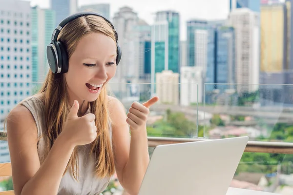 Jonge vrouw leert een vreemde taal of leert een vreemde taal op het Internet op haar balkon tegen de achtergrond van een grote stad. Online taal school levensstijl — Stockfoto