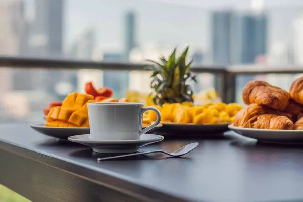Reggeliző asztal, kávé gyümölcs és kenyeret croisant, egy erkély, a nagy város a háttérben — Stock Fotó