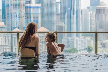 Anne ve oğlu mavi gökyüzünde şehir manzaralı açık yüzme havuzunda