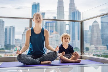 Anne ve oğlu büyük bir şehir arka planda balkonda yoga uygulamak. Spor anne çocukla sabah egzersiz evde yapıyor. Anne ve çocuk çalışmaları birlikte, sağlıklı aile yaşam yapmak