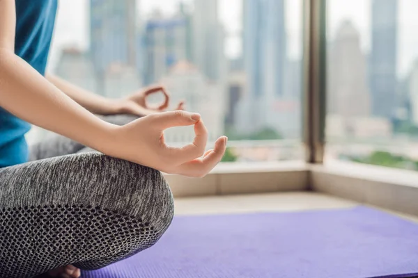 Young woman is practicing yoga in the morning on her balcony with a panoramic view of the city and skyscrapers — Stock Photo, Image