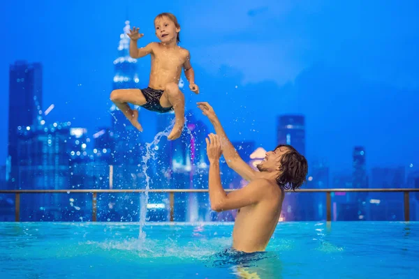 Padre e hijo en piscina al aire libre con vista a la ciudad en el cielo azul — Foto de Stock