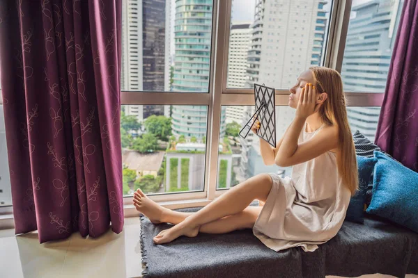 Giovane donna fa il trucco seduto vicino alla finestra con una vista panoramica dei grattacieli e la grande città — Foto Stock