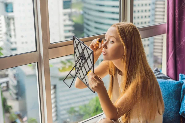 Mujer joven hace maquillaje sentado junto a la ventana con una vista panorámica de los rascacielos y la gran ciudad —  Fotos de Stock