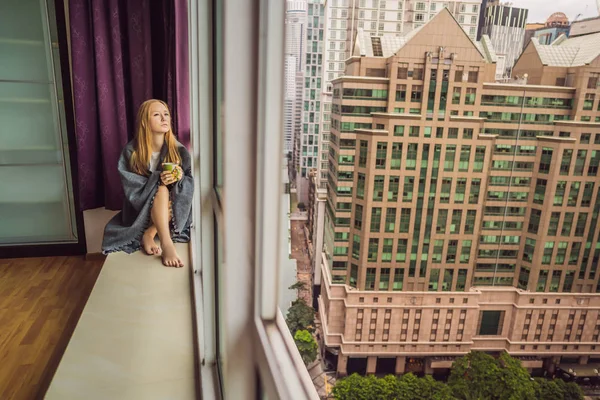 Женщина завернутая в одеяло и смотрящая на большой город — стоковое фото