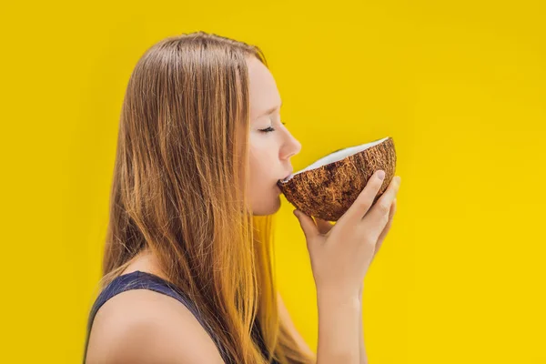 Jovem mulher bebendo leite de coco em Chafrom coco em um fundo amarelo — Fotografia de Stock