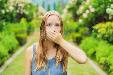 Genç ve güzel bir kadın çiçek açan ağacın önünde burnunu siliyor. Bahar alerjisi konsepti