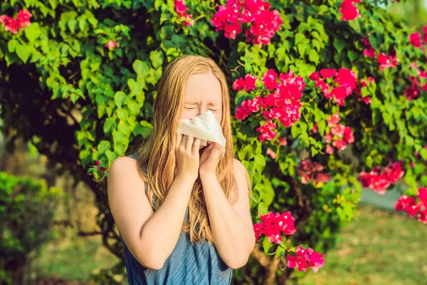 Ung vacker kvinna som blåser näsa framför blommande träd. Vårens allergikoncept — Stockfoto