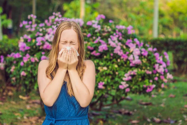 Genç ve güzel bir kadın çiçek açan ağacın önünde burnunu siliyor. Bahar alerjisi konsepti — Stok fotoğraf